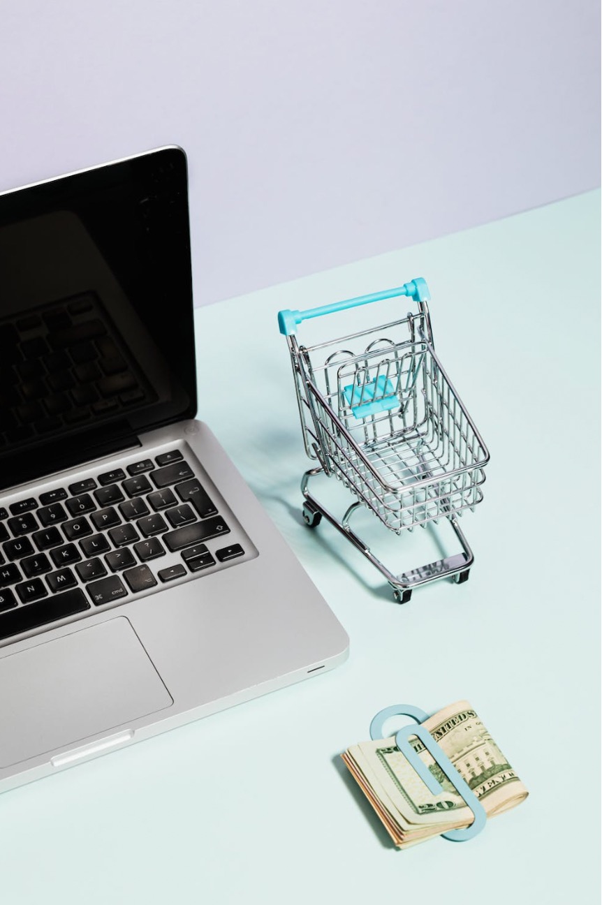 A Macbook Beside a Miniature Shopping Cart and Clipped Money
