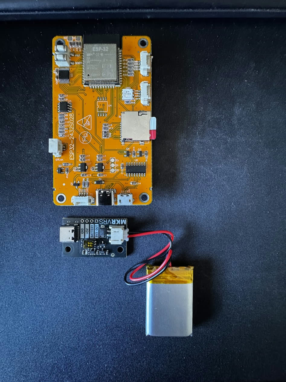ESP32 display board, charging module and lithium-polymer battery laid out on a desk
