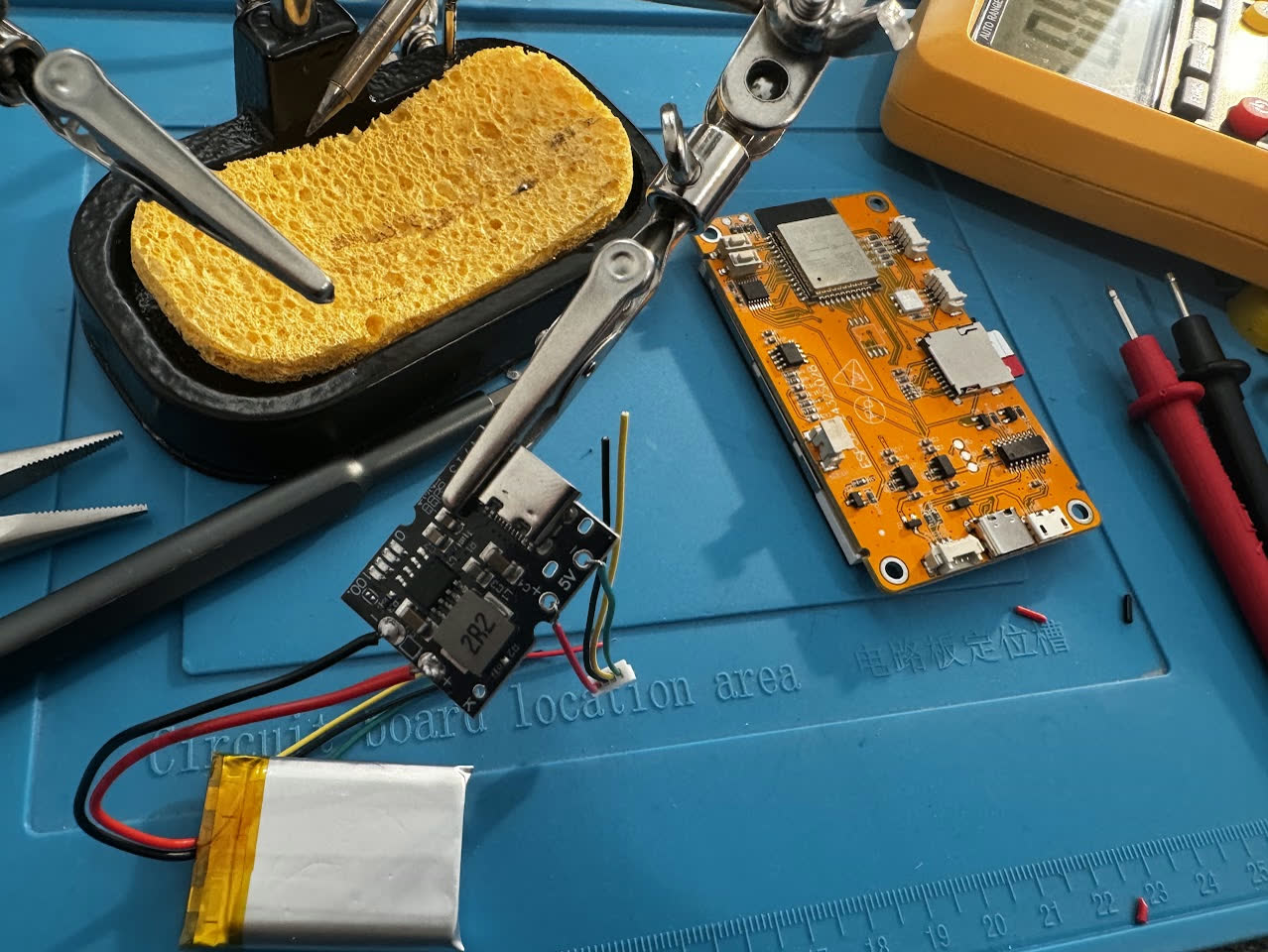 Charging module held in helping hands next to the ESP32 board and a soldering station